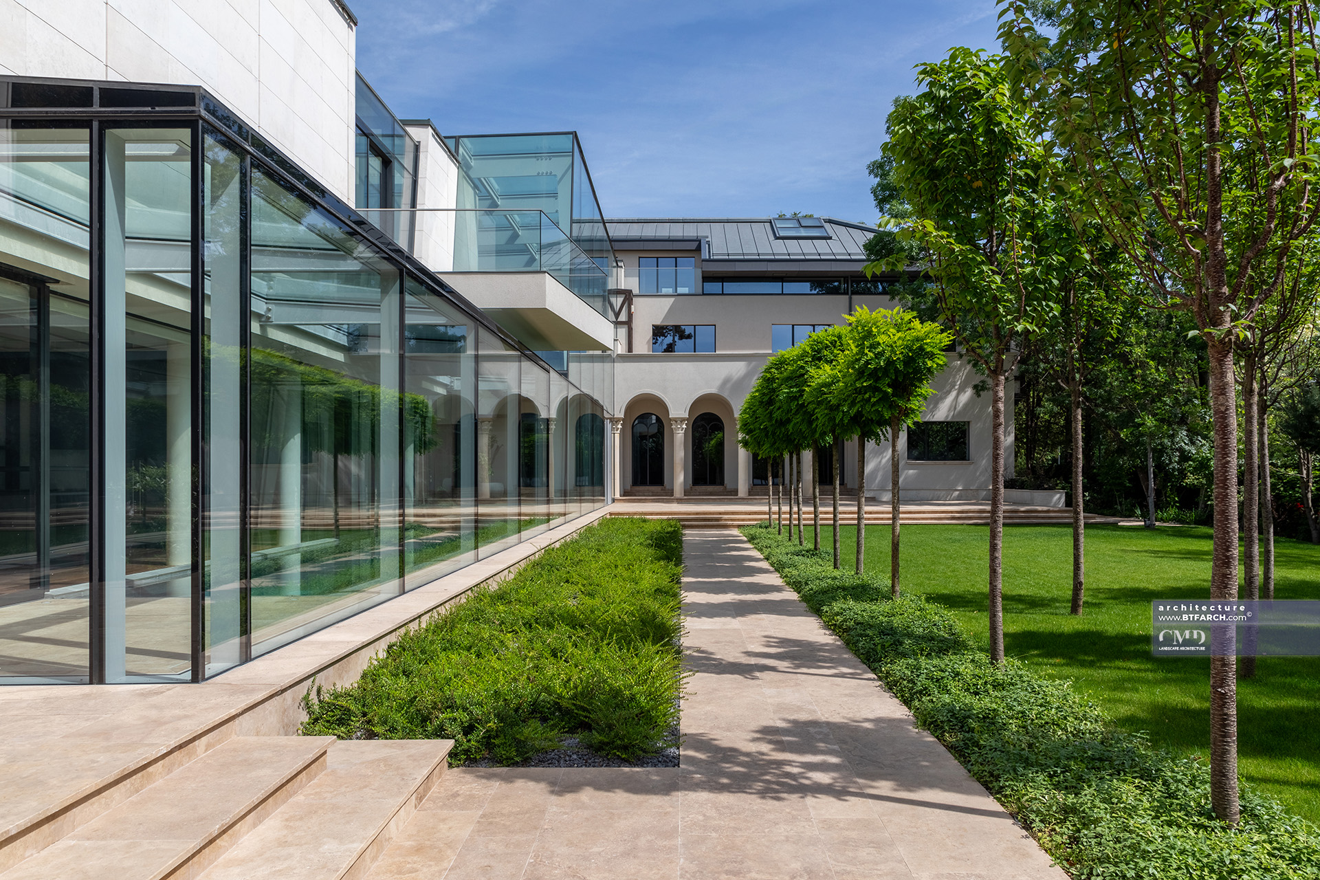 Axial garden pathway lined with trees, connecting glass conservatory to classical villa facade
